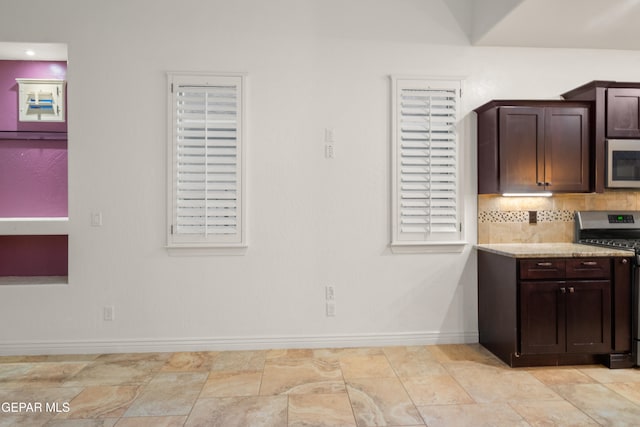 kitchen featuring appliances with stainless steel finishes, light stone counters, dark brown cabinets, and tasteful backsplash