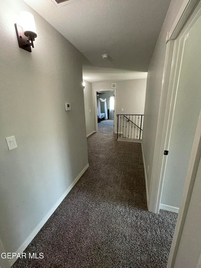 corridor featuring dark carpet and a textured ceiling