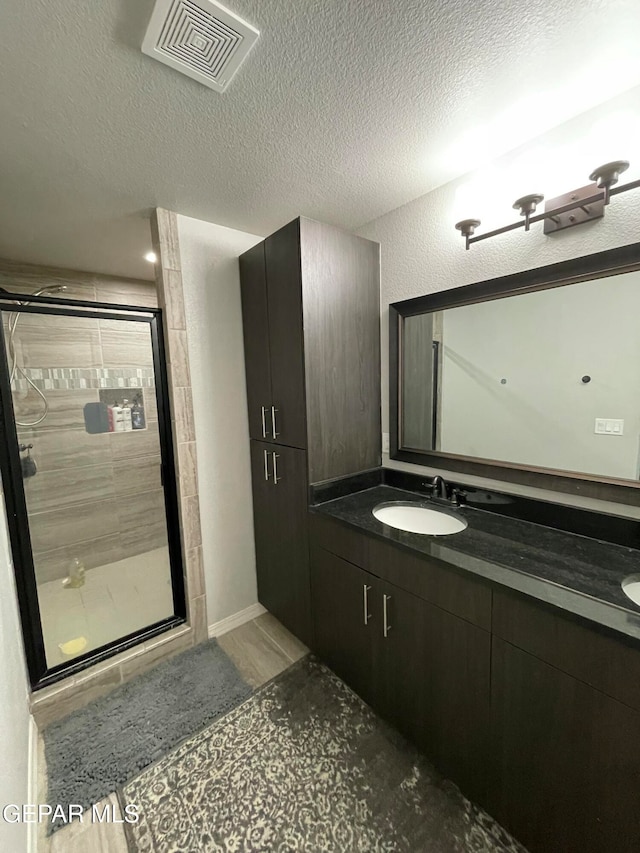 bathroom featuring vanity, a textured ceiling, and a shower with shower door