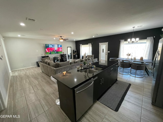 kitchen with appliances with stainless steel finishes, sink, ceiling fan with notable chandelier, pendant lighting, and a kitchen island with sink