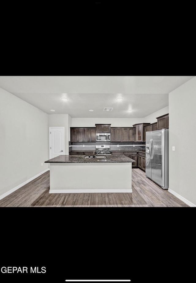 kitchen with appliances with stainless steel finishes, light hardwood / wood-style flooring, dark brown cabinets, and an island with sink