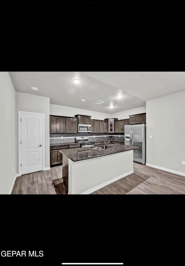 kitchen featuring tasteful backsplash, dark brown cabinets, a center island with sink, appliances with stainless steel finishes, and light hardwood / wood-style flooring