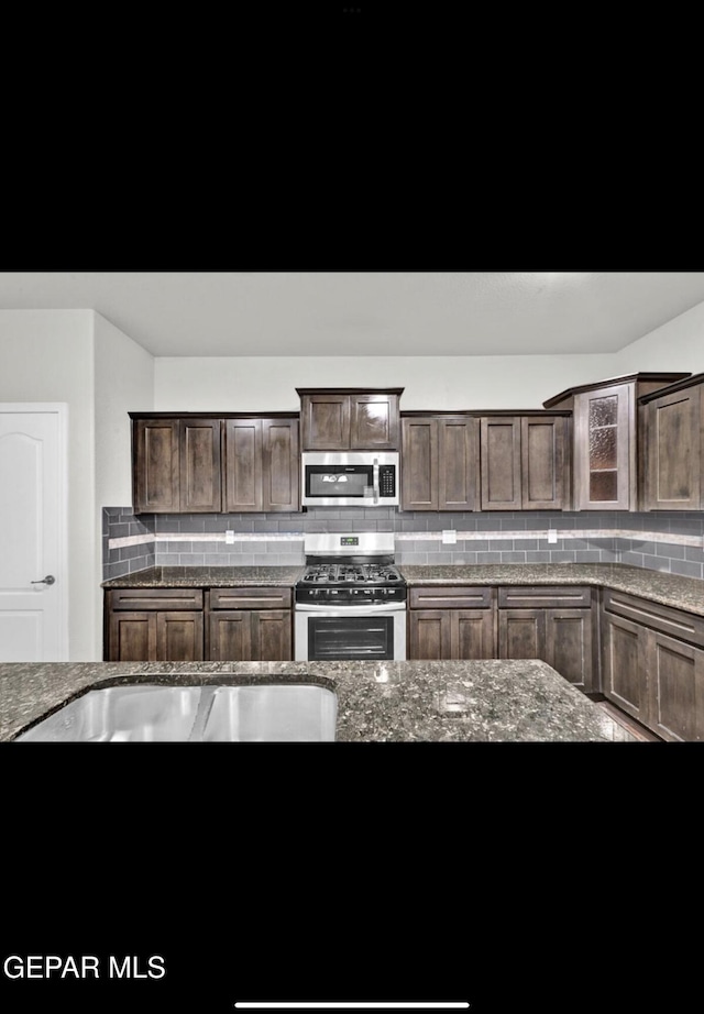 kitchen featuring appliances with stainless steel finishes, dark brown cabinetry, backsplash, and dark stone counters