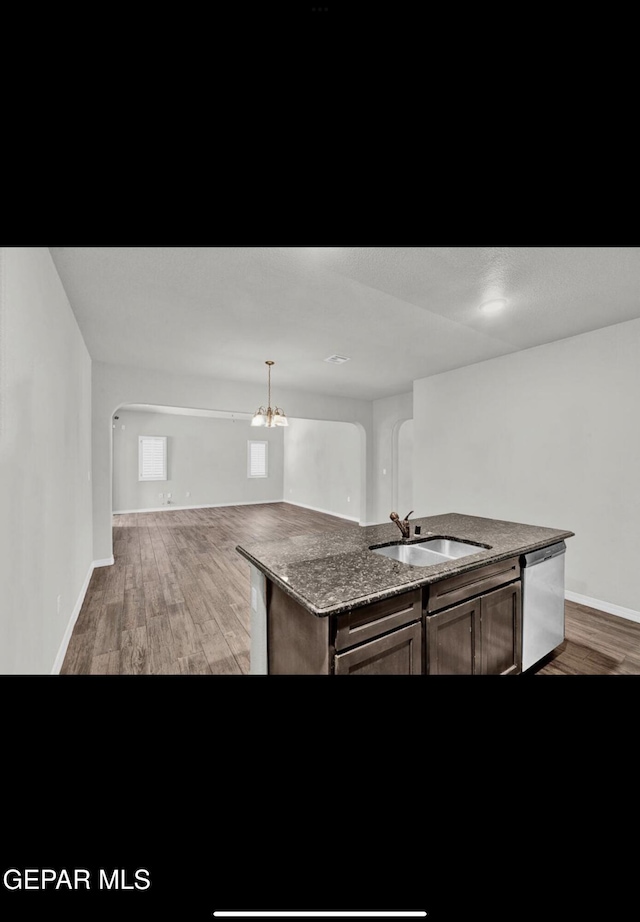 kitchen with wood-type flooring, sink, dishwasher, an island with sink, and dark stone countertops