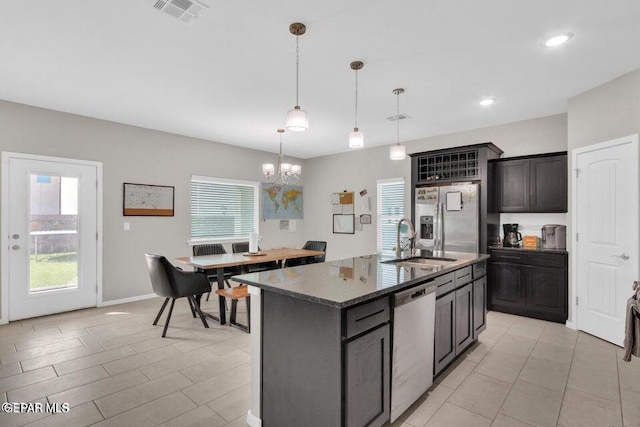 kitchen with a kitchen island with sink, dark stone counters, sink, pendant lighting, and appliances with stainless steel finishes