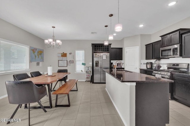 kitchen with appliances with stainless steel finishes, an inviting chandelier, a kitchen island with sink, sink, and decorative light fixtures