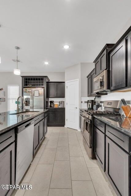 kitchen featuring light tile patterned floors, appliances with stainless steel finishes, dark stone countertops, pendant lighting, and sink