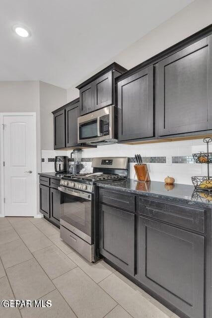 kitchen with light tile patterned flooring, dark stone countertops, and stainless steel appliances