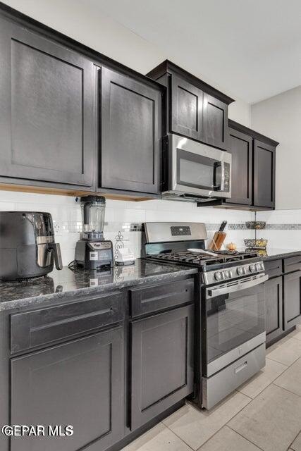 kitchen featuring dark stone countertops, backsplash, stainless steel appliances, and light tile patterned flooring