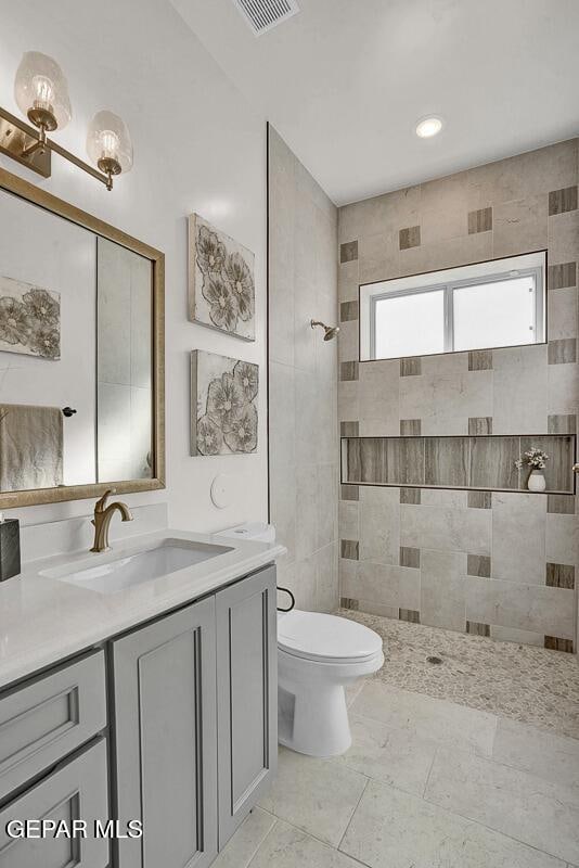 bathroom with a tile shower, toilet, tile walls, and vanity