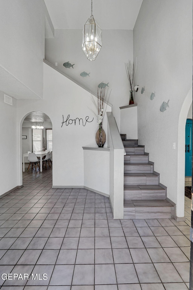 staircase featuring an inviting chandelier, a high ceiling, and tile patterned flooring