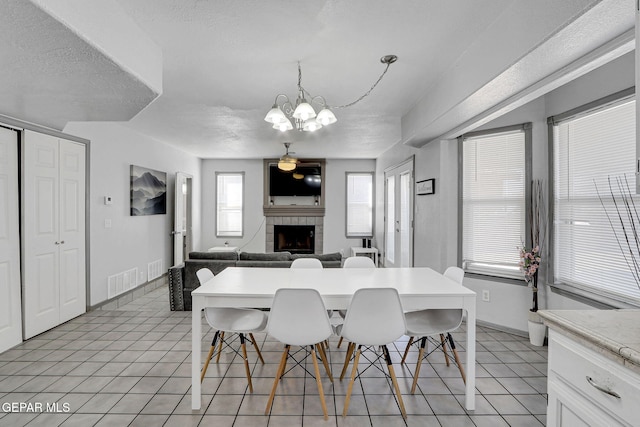 dining area featuring light tile patterned floors, a textured ceiling, a chandelier, and a tile fireplace