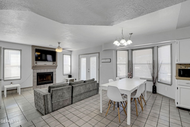 dining area featuring a healthy amount of sunlight, a textured ceiling, a fireplace, and ceiling fan with notable chandelier