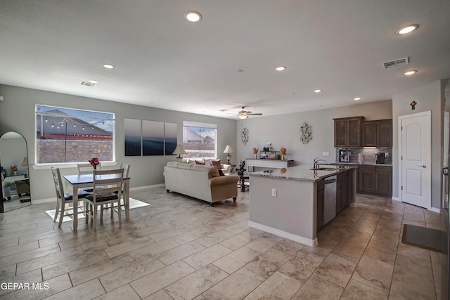 kitchen with sink, an island with sink, dark brown cabinets, ceiling fan, and stainless steel dishwasher