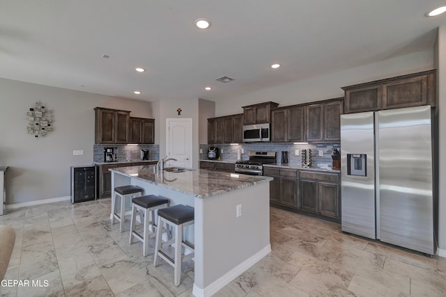 kitchen with decorative backsplash, an island with sink, a kitchen bar, dark stone countertops, and stainless steel appliances