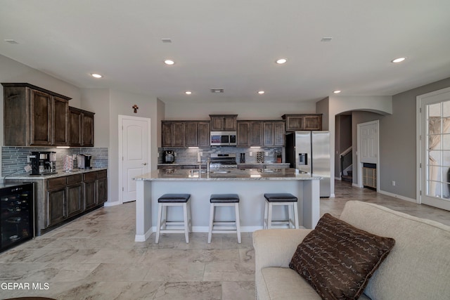 kitchen with wine cooler, stainless steel appliances, dark brown cabinets, and an island with sink