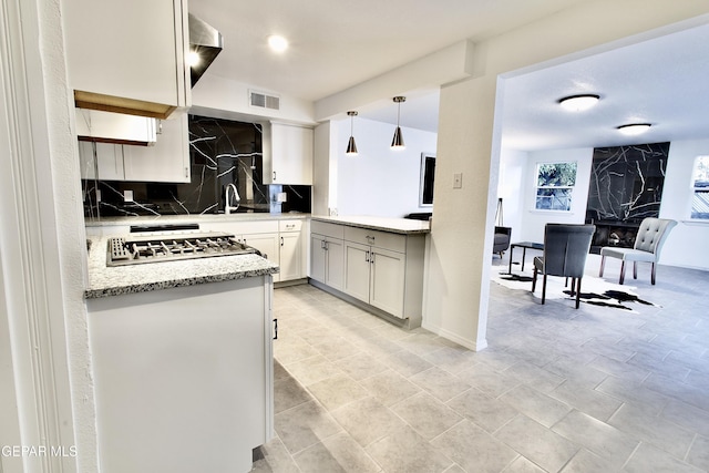 kitchen with decorative backsplash, light stone countertops, decorative light fixtures, white cabinets, and stainless steel gas stovetop