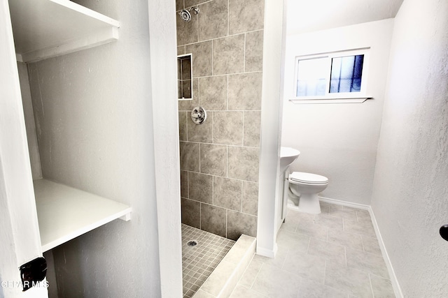 bathroom featuring tile patterned flooring, toilet, and a tile shower