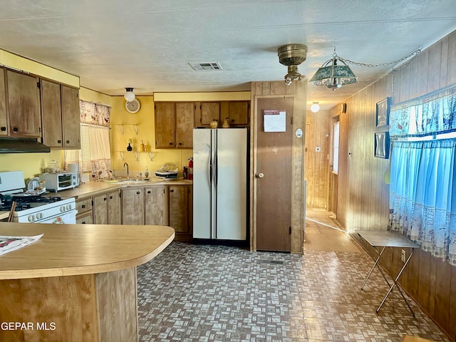 kitchen featuring white gas range oven, kitchen peninsula, wood walls, sink, and stainless steel fridge