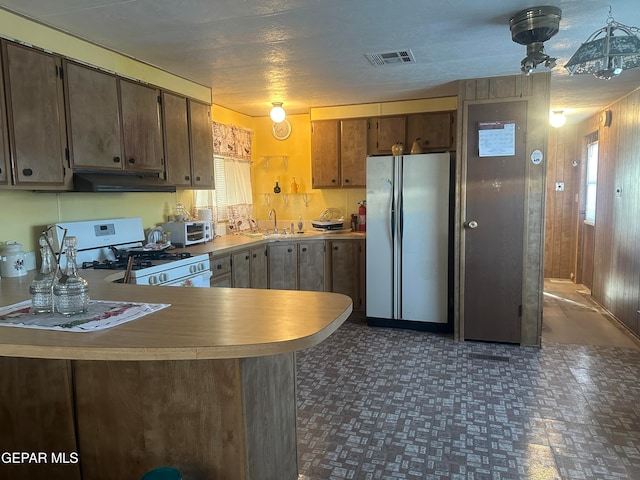 kitchen with white gas stove, stainless steel refrigerator, sink, kitchen peninsula, and a textured ceiling