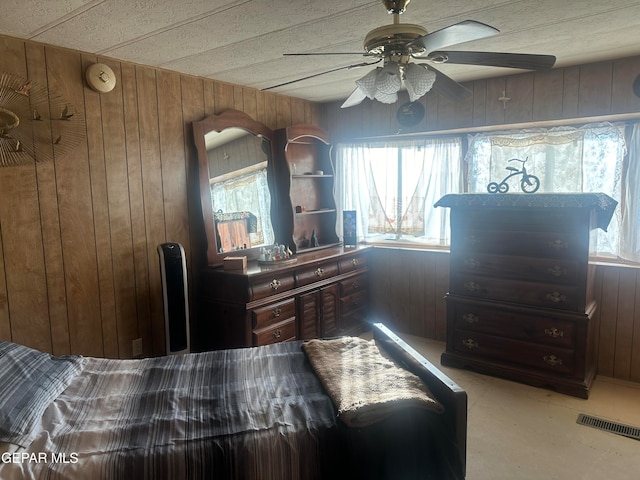 bedroom with ceiling fan, multiple windows, and wooden walls