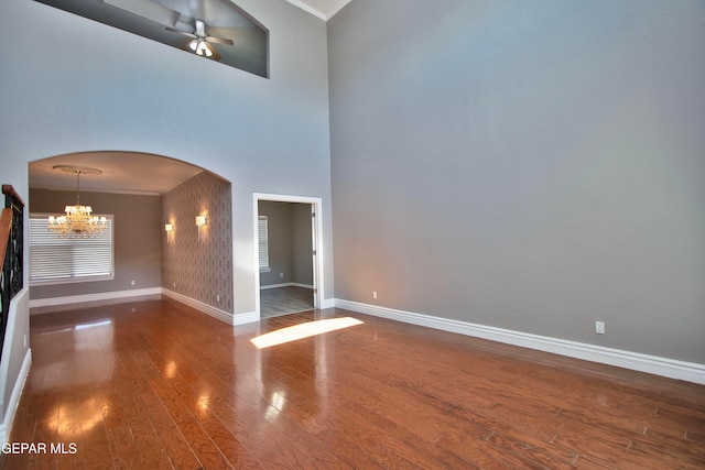 spare room with a high ceiling, ornamental molding, hardwood / wood-style flooring, and ceiling fan with notable chandelier