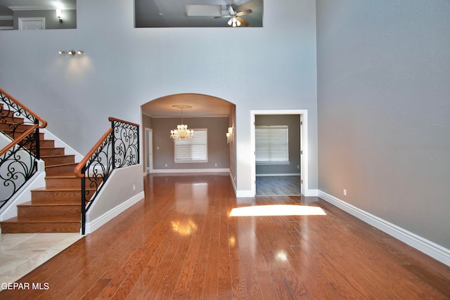 foyer featuring a high ceiling, ornamental molding, hardwood / wood-style flooring, and ceiling fan with notable chandelier