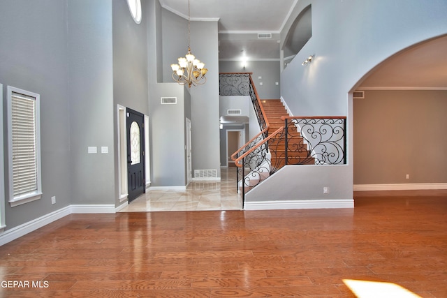 foyer entrance with a notable chandelier, ornamental molding, a high ceiling, and hardwood / wood-style floors