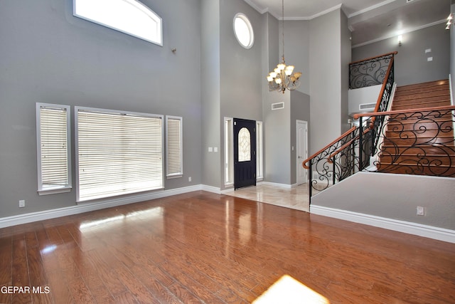 entrance foyer with crown molding, a notable chandelier, a towering ceiling, and light hardwood / wood-style flooring