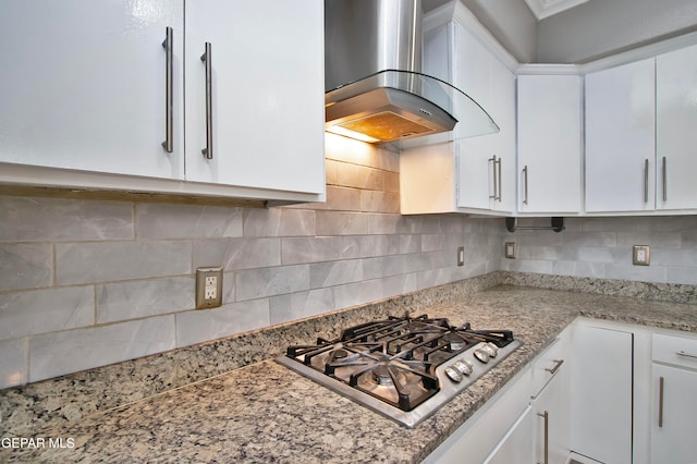 kitchen with light stone counters, white cabinetry, wall chimney range hood, and backsplash