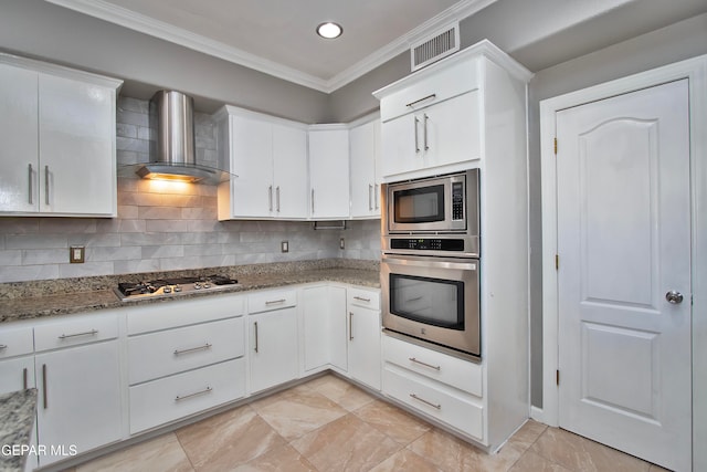 kitchen with appliances with stainless steel finishes, white cabinetry, light stone countertops, ornamental molding, and wall chimney exhaust hood