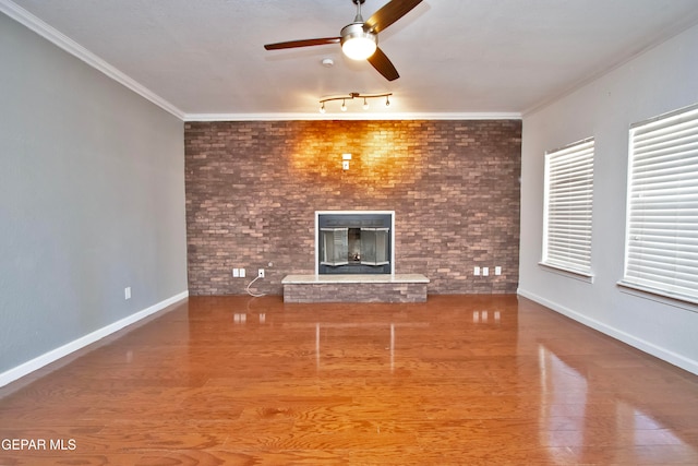 unfurnished living room featuring wood-type flooring, ornamental molding, brick wall, a brick fireplace, and ceiling fan