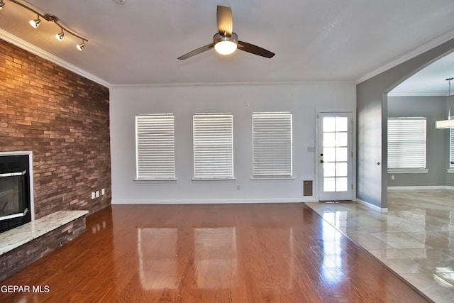 unfurnished living room featuring a fireplace, hardwood / wood-style floors, ceiling fan, brick wall, and ornamental molding