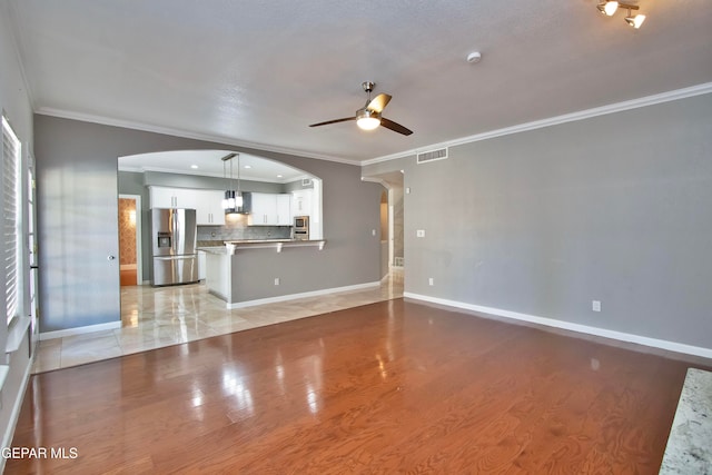 unfurnished living room featuring ceiling fan, ornamental molding, and light wood-type flooring