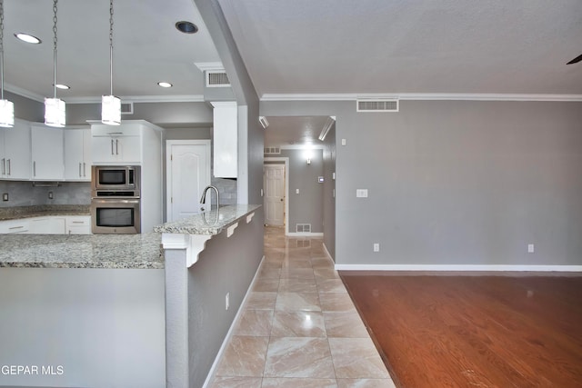 kitchen featuring light stone counters, appliances with stainless steel finishes, white cabinetry, ornamental molding, and decorative light fixtures