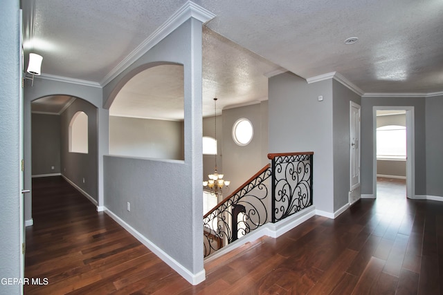 hallway featuring dark wood-type flooring, a textured ceiling, crown molding, and an inviting chandelier