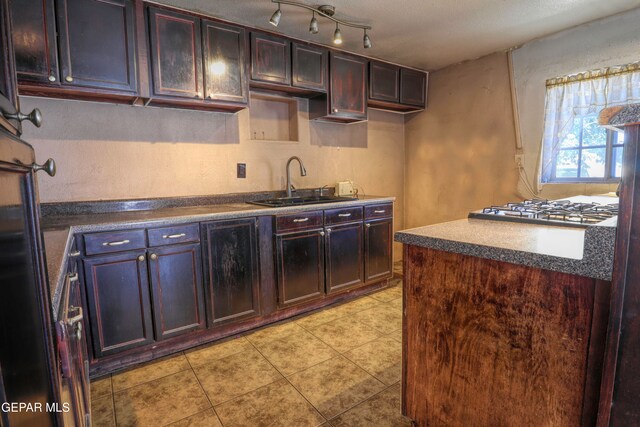 kitchen with stainless steel gas cooktop, dark brown cabinetry, sink, and light tile patterned floors