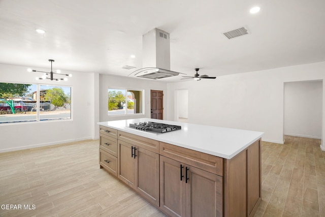 kitchen with exhaust hood, a kitchen island, stainless steel gas stovetop, light hardwood / wood-style floors, and decorative light fixtures