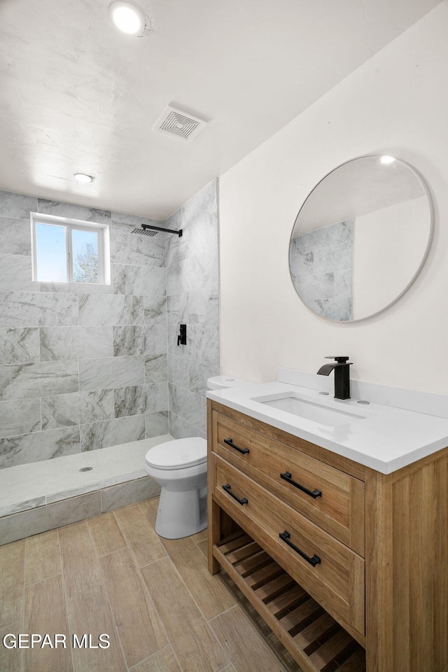 bathroom featuring toilet, vanity, and tiled shower