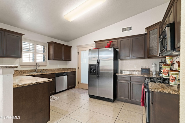 kitchen with lofted ceiling, light stone counters, light tile patterned floors, dark brown cabinetry, and stainless steel appliances