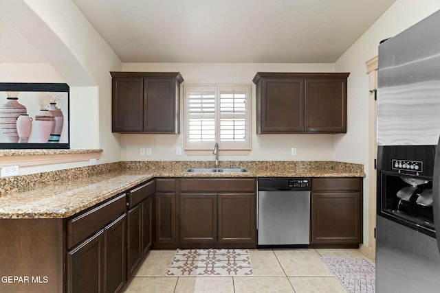 kitchen with dark brown cabinets, light tile patterned floors, appliances with stainless steel finishes, light stone countertops, and sink