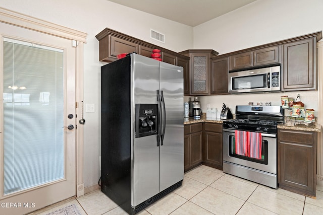 kitchen featuring light stone countertops, appliances with stainless steel finishes, dark brown cabinetry, and light tile patterned floors