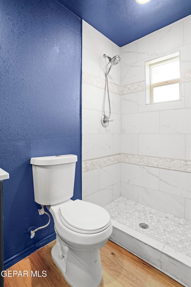 bathroom with a tile shower, toilet, a textured ceiling, and hardwood / wood-style floors