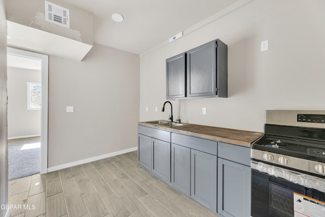 kitchen with wooden counters, gray cabinetry, stainless steel stove, sink, and light hardwood / wood-style floors