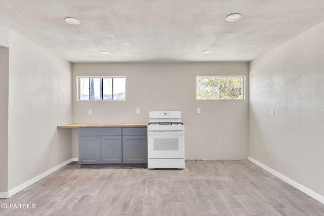 kitchen featuring a textured ceiling, gray cabinetry, light wood-type flooring, and white gas range