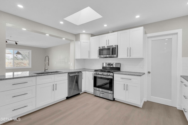 kitchen featuring tasteful backsplash, appliances with stainless steel finishes, white cabinetry, light hardwood / wood-style flooring, and sink