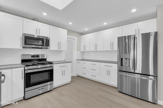 kitchen with appliances with stainless steel finishes, white cabinets, tasteful backsplash, and light hardwood / wood-style floors