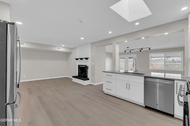 kitchen with stainless steel appliances, sink, a brick fireplace, white cabinetry, and light stone counters