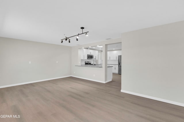 unfurnished living room featuring sink, dark wood-type flooring, and rail lighting