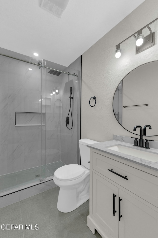 bathroom featuring toilet, a shower with shower door, vanity, and tile patterned floors